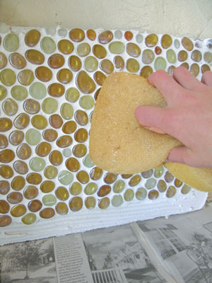 6. Let the grout set up for about 30 minutes, then gently remove the grout from the face of the glass with a damp sponge. Rinse the sponge frequently. When the grout dries, buff your new backsplash with a soft cloth to remove any remaining haze from the grout. Use a grout sealer (we used AFM Safecoat Grout Sealer) to protect your new mosaic.